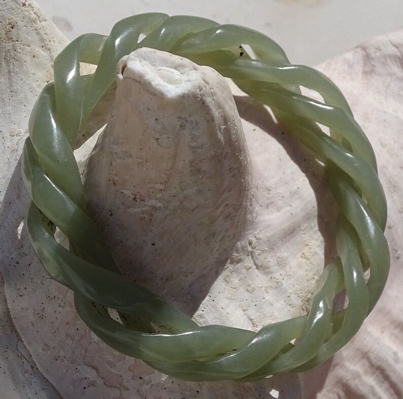 May include: A green jade bracelet with a braided design. The bracelet is made of a smooth, polished jade and has a natural green color.