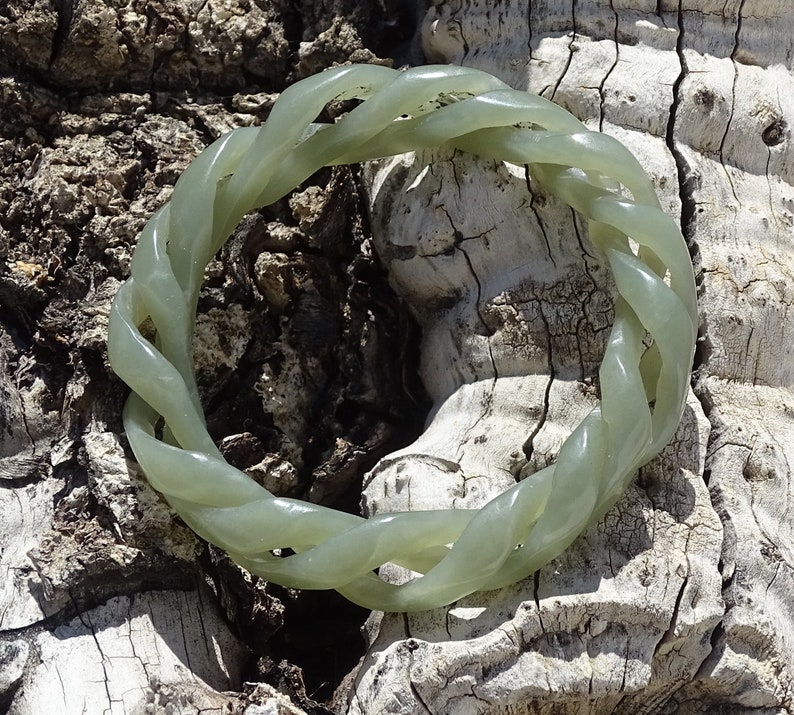 May include: A green jade bracelet with a braided design. The bracelet is made of a smooth, polished jade and has a natural, earthy look.