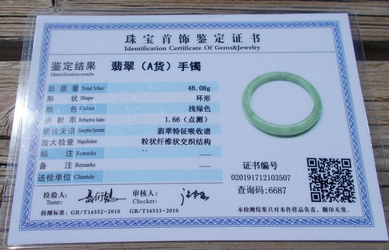 May include: A jadeite jade bracelet with a light green colour. The bracelet weighs 48.08 grams and has a certificate of authenticity with a unique identification number and a QR code. The certificate states that the bracelet is made of type A jadeite jade.