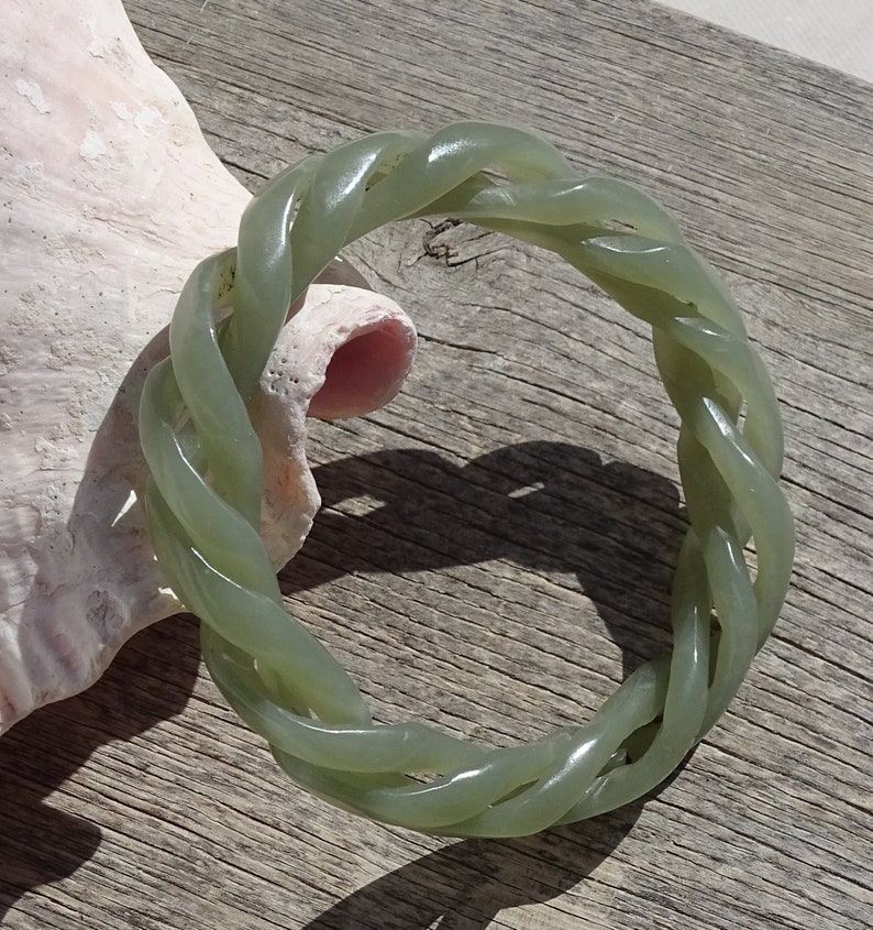 May include: A green jade bangle bracelet with a braided design. The bracelet is made of a smooth, polished jade and has a natural, earthy look.