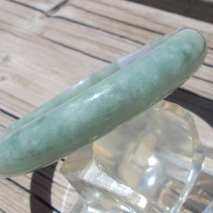 May include: A light green jade bangle bracelet. The bracelet is smooth and polished, with a subtle marbled pattern.