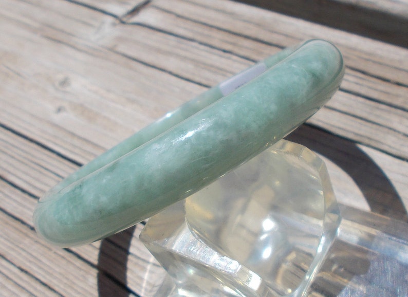 May include: A light green jade bangle bracelet. The bracelet is smooth and polished, with a subtle marbled pattern.