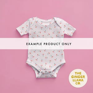 May include: White baby onesie with a pattern of red and pink cherries. The onesie has short sleeves and snaps at the bottom. The text "EXAMPLE PRODUCT ONLY" is across the front. A circular logo with the text "THE GINGER LLAMA CO." is in the bottom right corner.