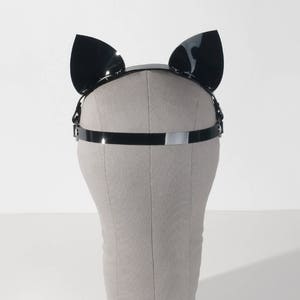 May include: Black cat ears headband with a silver metal band. The headband is on a white mannequin head.