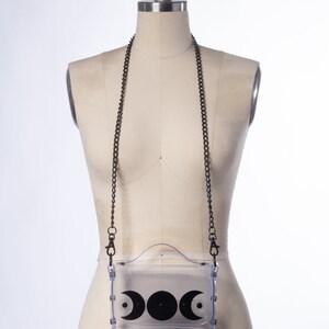 May include: A clear plastic crossbody bag with a black chain strap and a black crescent moon design.