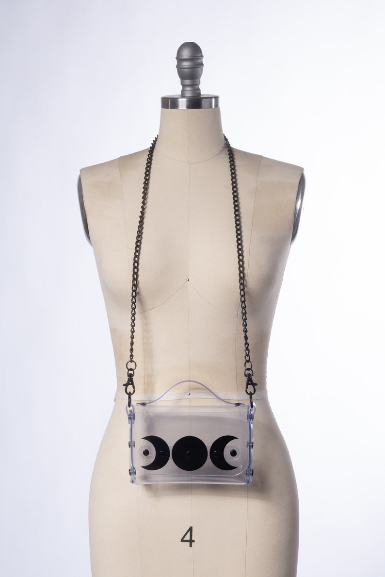May include: A clear plastic crossbody bag with a black chain strap and a black crescent moon design.
