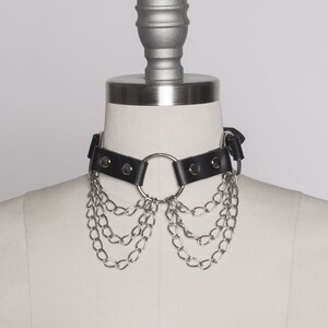 May include: A black leather choker with a silver ring and multiple silver chains hanging from it.