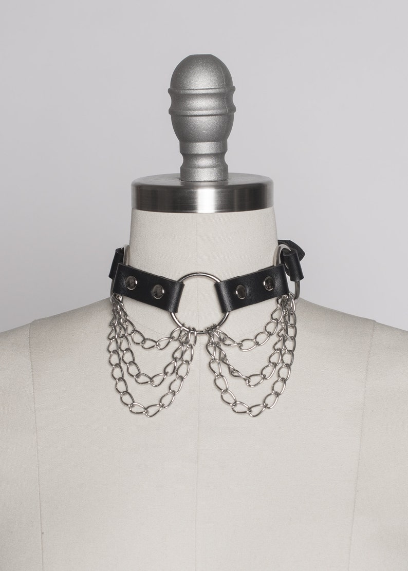 May include: A black leather choker with a silver ring and multiple silver chains hanging from it.