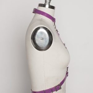 May include: Purple latex harness with a choker and a belt. The harness has silver hardware and is adjustable.