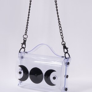 May include: A clear plastic crossbody bag with a black chain strap and three black crescent moon shapes on the front.