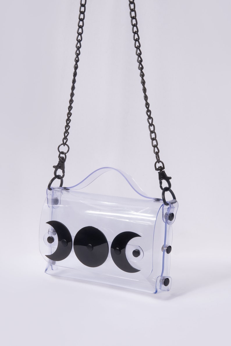 May include: A clear plastic crossbody bag with a black chain strap and three black crescent moon shapes on the front.