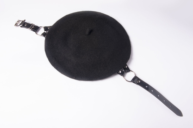 May include: A black beret with a black leather strap and silver metal hardware.