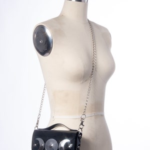 May include: A black patent leather crossbody bag with a silver chain strap and three silver crescent moon embellishments.