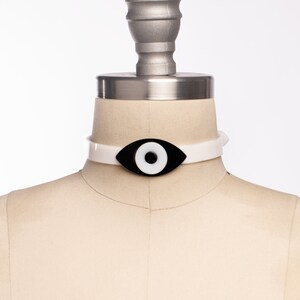 May include: White choker necklace with a black and white evil eye charm.