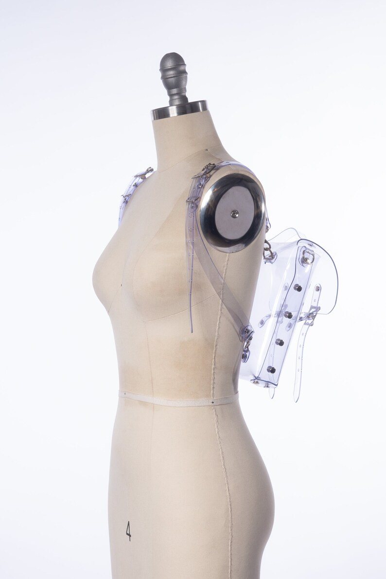 Puede incluir: Una mochila transparente de pl&aacute;stico con correas ajustables y hebillas plateadas. La mochila est&aacute; en un maniqu&iacute; blanco.