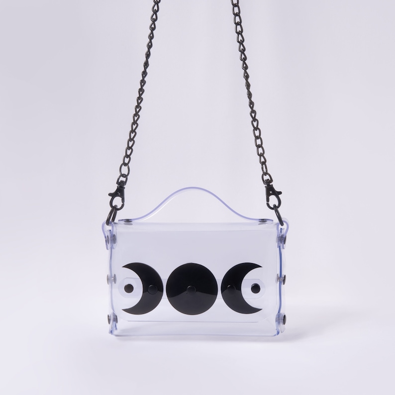 May include: A clear plastic crossbody bag with a black chain strap and three black crescent moon designs on the front.