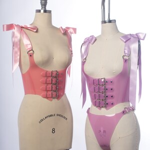 Pastel pink pvc buckle bodice with satin ribbon ties on the left, pastel purple lavender pvc buckle bodice and harness thong on the left, displayed on a dress form.