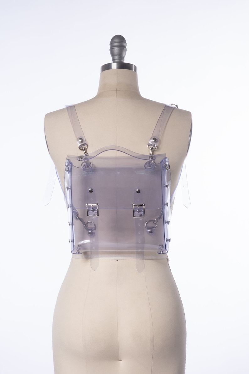 Puede incluir: Una mochila transparente de pl&aacute;stico con herrajes plateados y correas ajustables. La mochila est&aacute; en un maniqu&iacute; blanco.
