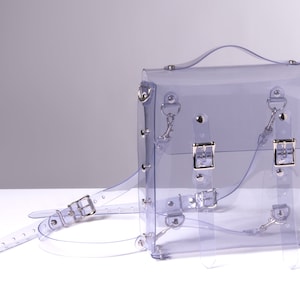 Puede incluir: Una mochila transparente de pl&aacute;stico con hebillas y herrajes plateados. La mochila tiene correas ajustables y un asa superior.