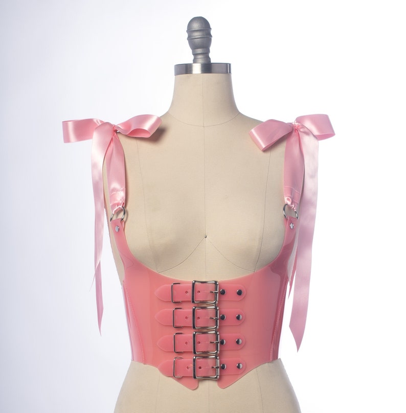 Pastel pink pvc buckle bodice with satin ribbon ties, displayed on a dress form.