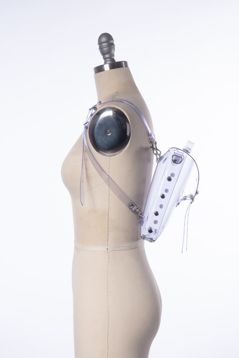 Puede incluir: Una mochila transparente de pl&aacute;stico con herrajes plateados y una correa de cadena. La mochila se lleva puesta en un maniqu&iacute;.