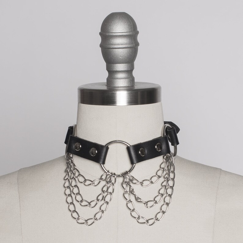 May include: A black leather choker with a silver ring and multiple silver chains hanging from it.