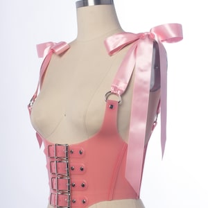 Pastel pink pvc buckle bodice with satin ribbon ties, displayed on a dress form.