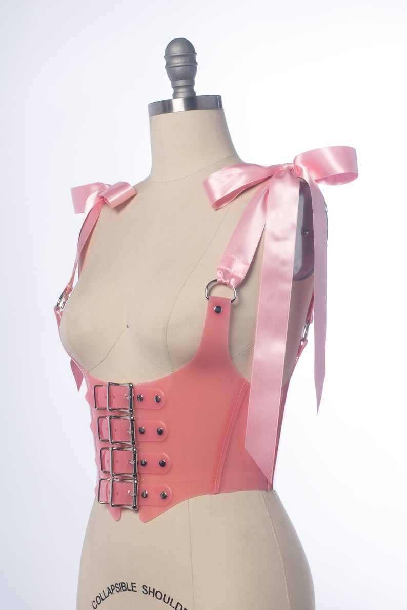 Pastel pink pvc buckle bodice with satin ribbon ties, displayed on a dress form.