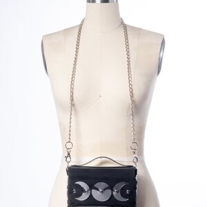 May include: A black faux leather crossbody bag with a silver chain strap and three silver crescent moon embellishments.
