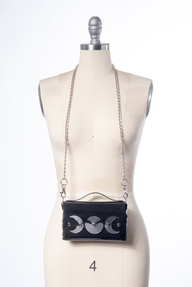May include: A black faux leather crossbody bag with a silver chain strap and three silver crescent moon embellishments.