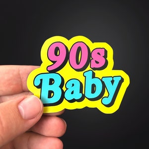 Pode incluir: Um adesivo amarelo com o texto "90s Baby" em letras rosa e azul.