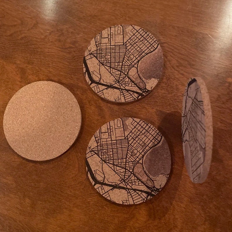 May include: Set of four cork coasters featuring a city map design. The coasters are round and have a brown cork surface with a black map printed on top.