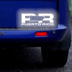 Pode incluir: Um adesivo branco na parte de trás de um carro azul com as letras "PR" e as palavras "PUERTO RICO" abaixo. O "P" de "PR" é substituído por um contorno da ilha de Porto Rico.