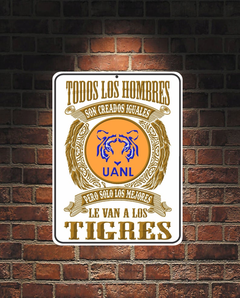 May include: A white metal sign with gold lettering and a tiger logo. The sign reads "Todos los hombres son creados iguales pero solo los mejores le van a los Tigres".