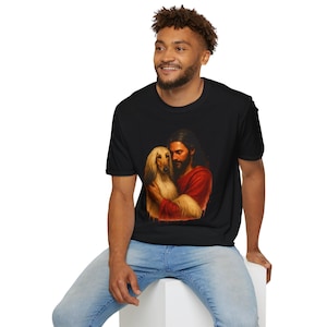 May include: A black t-shirt with a graphic print of Jesus holding a dog. The dog is a light brown Afghan Hound. The graphic is in a painting style.