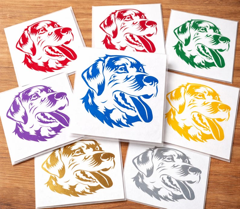 May include: A collection of square white cards featuring a stylized dog head in various colors, including red, blue, green, yellow, purple, gold, and gray. The dog's tongue is visible. The cards are arranged on a wooden surface.