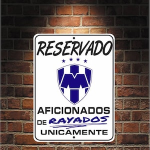 May include: A rectangular white sign with black text and a blue and white emblem. The sign reads "RESERVADO" above a shield-shaped logo and "AFICIONADOS DE RAYADOS UNICAMENTE" below. The sign is mounted on a brick wall.