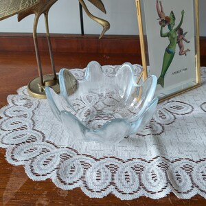 Pode incluir: Uma taça de vidro transparente com uma borda ondulada e festonada e um acabamento fosco e texturizado. A taça apresenta um design largo e aberto com vários picos arredondados ao longo da borda, criando uma forma semelhante a uma flor.