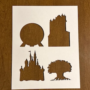 May include: A white paper stencil featuring four cut-out designs: a large sphere, a tall building, a castle with turrets, and a tree with roots. The designs are in silhouette form, perfect for crafting projects.