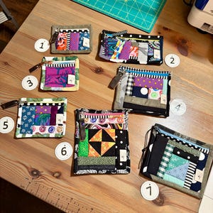 May include: A collection of seven small, handmade fabric wallets with various colorful patchwork designs. Each wallet features a zipper or drawstring closure and a unique combination of patterns and textures, including floral, geometric, and striped fabrics.
