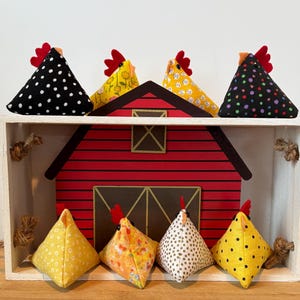 May include: A red barn with a white trim sits on a shelf with seven fabric chickens. The chickens are in various patterns of black and white polka dots, yellow and white polka dots, yellow and white floral, and brown and white polka dots.