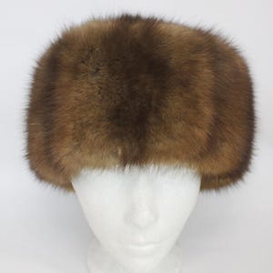 Puede incluir: Un sombrero de piel marrón con una corona redondeada. El sombrero se exhibe sobre una cabeza de maniquí blanca sobre un fondo blanco. La piel parece suave y tiene diferentes tonos de marrón.