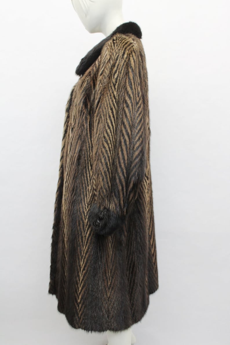 K&ouml;nnte beinhalten: Ein brauner und schwarzer Pelzmantel mit Chevron-Muster. Der Mantel hat einen schwarzen Pelzkragen und &Auml;rmelb&uuml;ndchen.