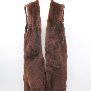 May include: A long brown faux fur vest with a shawl collar. The vest is sleeveless and has a straight hem.