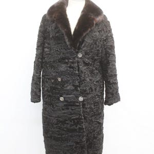 Può includere: Un lungo cappotto di pelliccia nero con collo in pelliccia marrone scuro. Il cappotto ha una superficie strutturata ed è allacciato con tre bottoni argentati. Il cappotto è esposto su un manichino bianco.