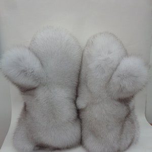 May include: A pair of light gray fur mittens. Each mitten has a rounded shape with a fluffy pom-pom detail on the side. The fur appears soft and luxurious, suggesting a winter accessory.