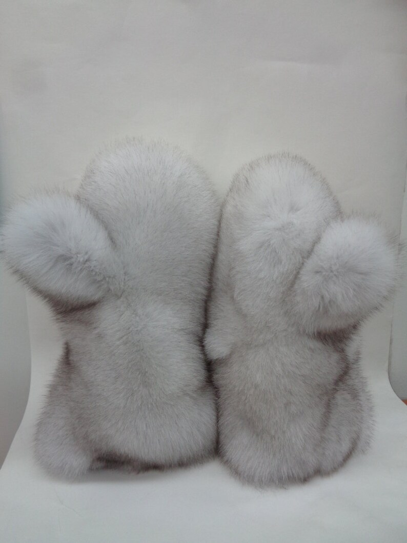 May include: A pair of light gray fur mittens. Each mitten has a rounded shape with a fluffy pom-pom detail on the side. The fur appears soft and luxurious, suggesting a winter accessory.