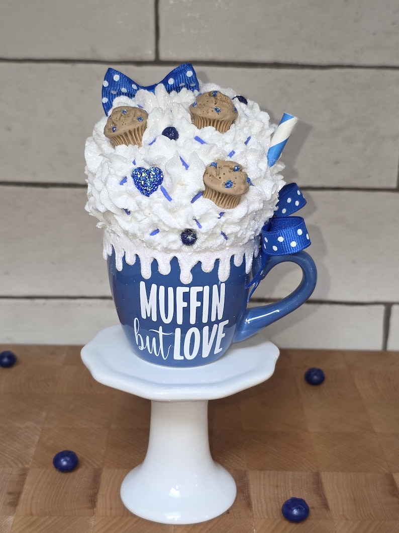 Close-up of hand-placed sprinkles and faux blueberries on handmade fake bake muffin display piece.