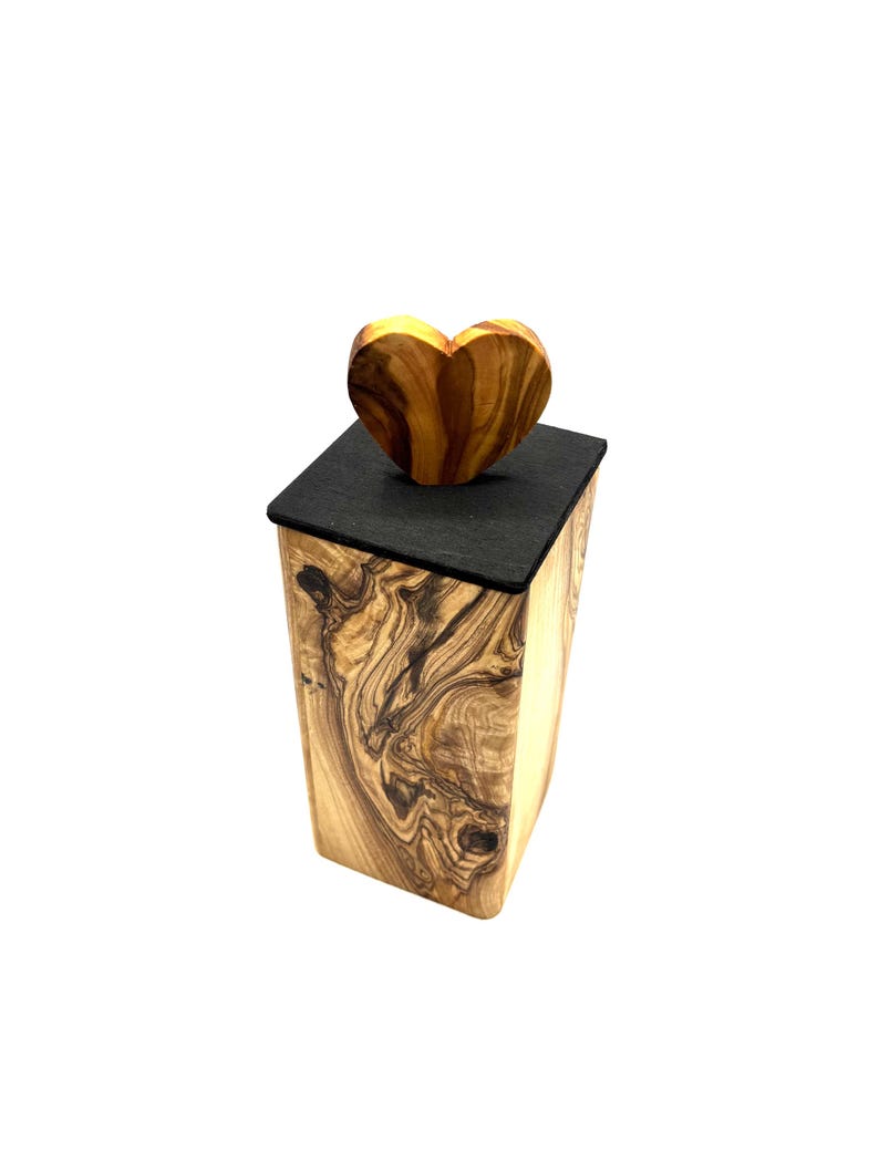 May include: A wooden box with a heart-shaped lid. The box is made of light-colored wood with dark, swirling grain patterns. The lid is a dark gray color, and the heart-shaped top is made of the same wood as the box.