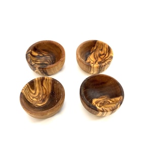 Peut inclure: Quatre petits bols ronds en bois avec un motif de grain de bois naturel. Les bols sont en bois d'olivier et ont une couleur brun foncé avec des stries brun clair.